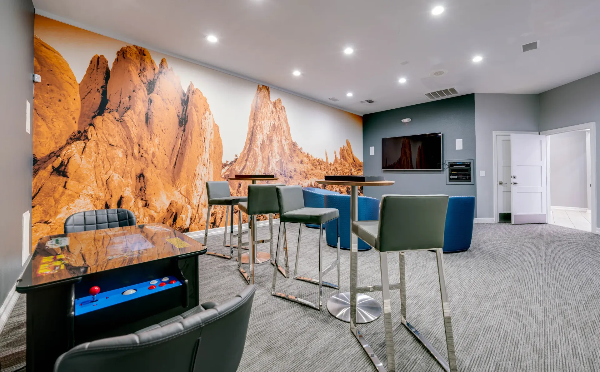 Community room with a large mural of rocky mountains, bar seating, and an arcade table.