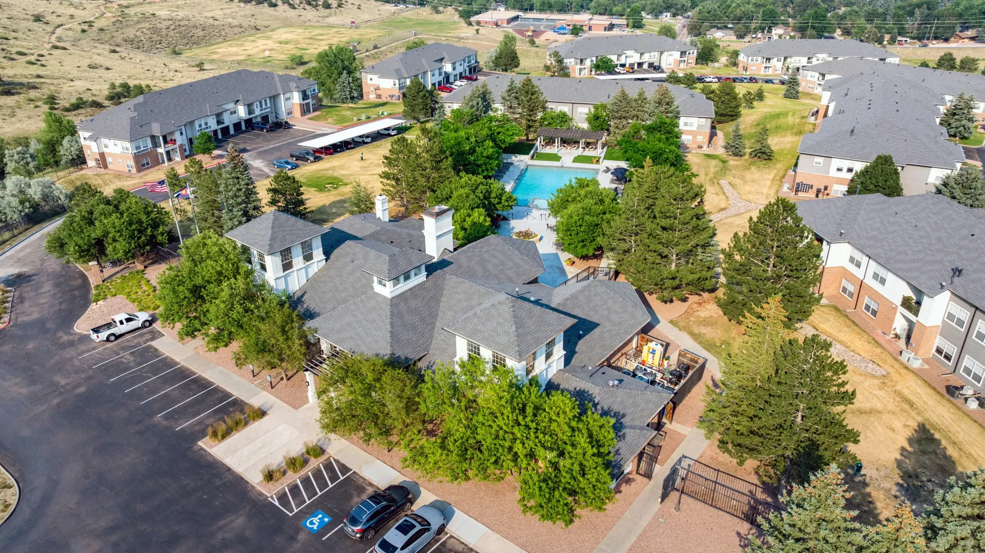 Aerial view of a multifamily apartment complex featuring a swimming pool, clubhouse, and surrounding buildings.
