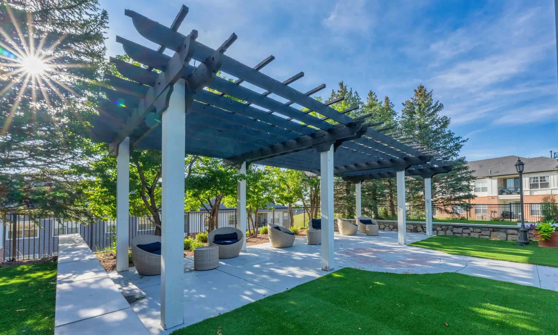 Outdoor pergola with seating and green space.