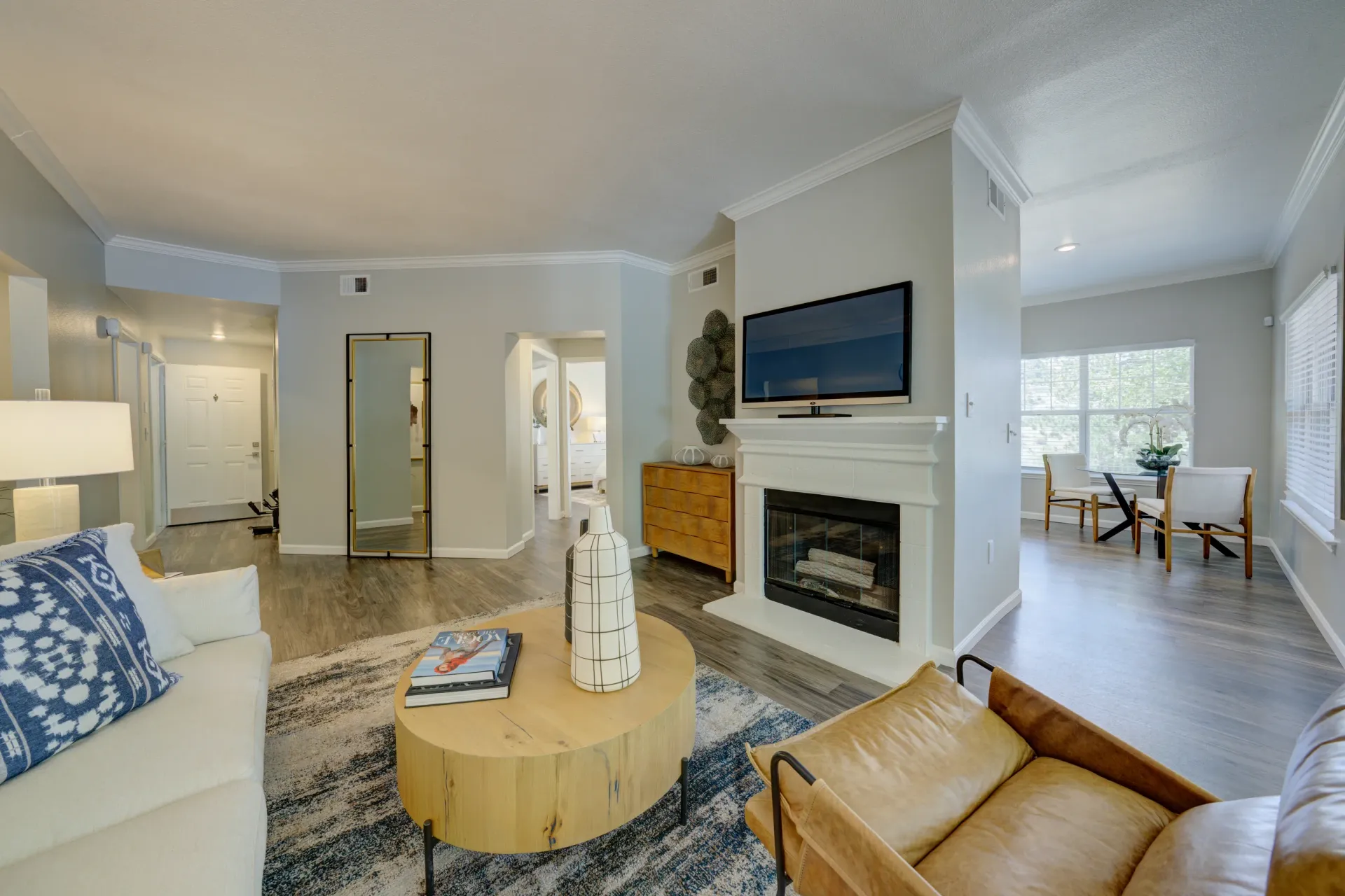 Living room with fireplace, TV, couch, coffee table, and dining area in background.