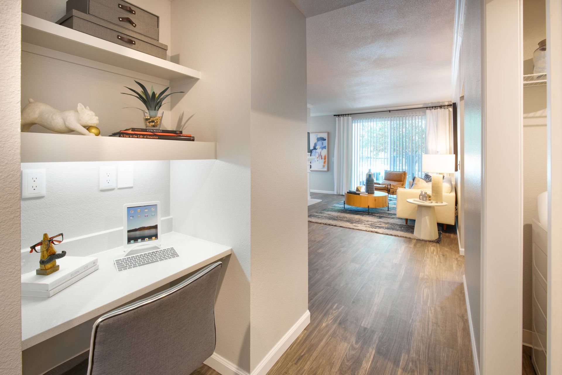 Built-in white desk with laptop and shelves in a hallway leading to a living area.