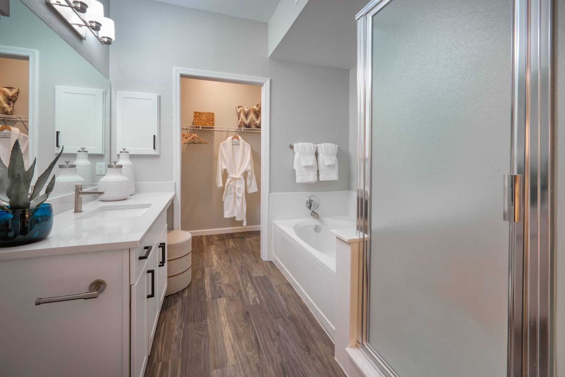 Bathroom in an apartment with a white vanity, mirror, tub/shower, and a closet visible through the doorway.