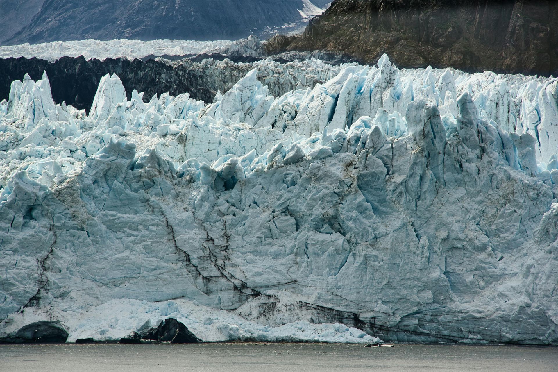 Jagged blue-white glacier with dark mountain backdrop and water in front
