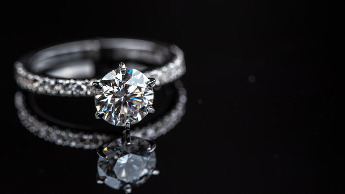 A close up of a diamond ring and a wedding ring on a black surface.