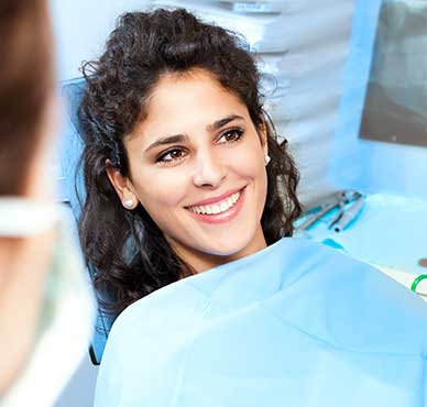 Una persona sonriente sentada en un sillón dental con un babero protector azul.