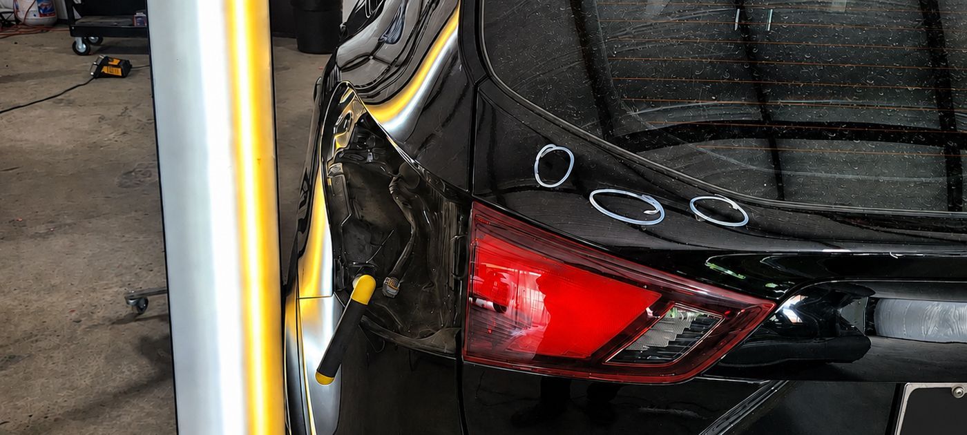 Rear of a black car with a damaged red taillight beside a yellow post in a garage
