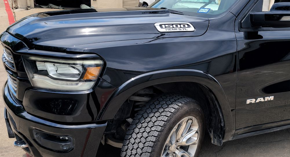 Close-up of a black RAM pickup truck’s front side and wheel, parked outdoors.