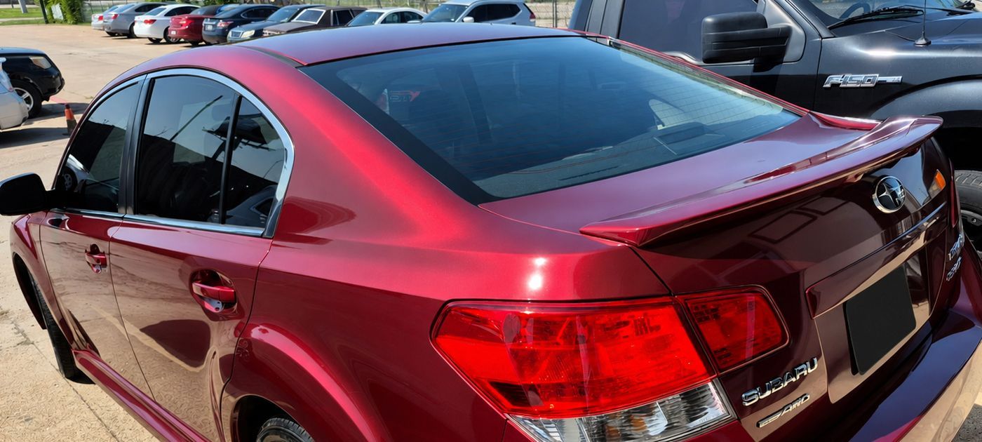 Maroon sedan parked outdoors in a lot, seen from the rear side.