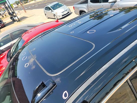 Top view of a dark blue car roof with white marker circles, parked next to a red car outside.
