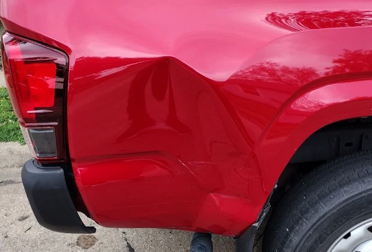 Red pickup truck with a large dent in the rear side panel near the wheel