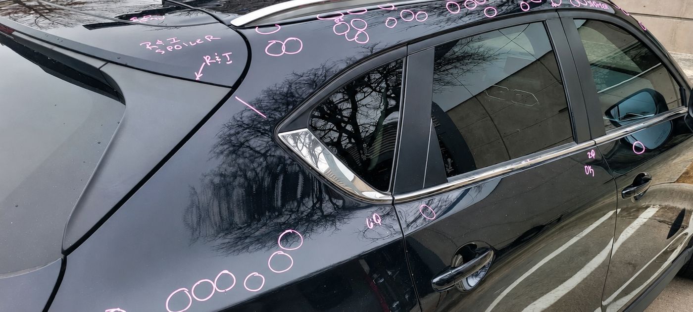 Black car with pink chalk markings on the windows and body in a parking lot