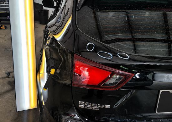 Black Nissan SUV rear bumper scrapes a yellow bollard in a parking lot