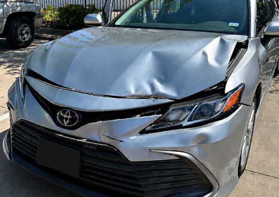 Damaged silver Toyota sedan with a crumpled hood and front-end collision damage