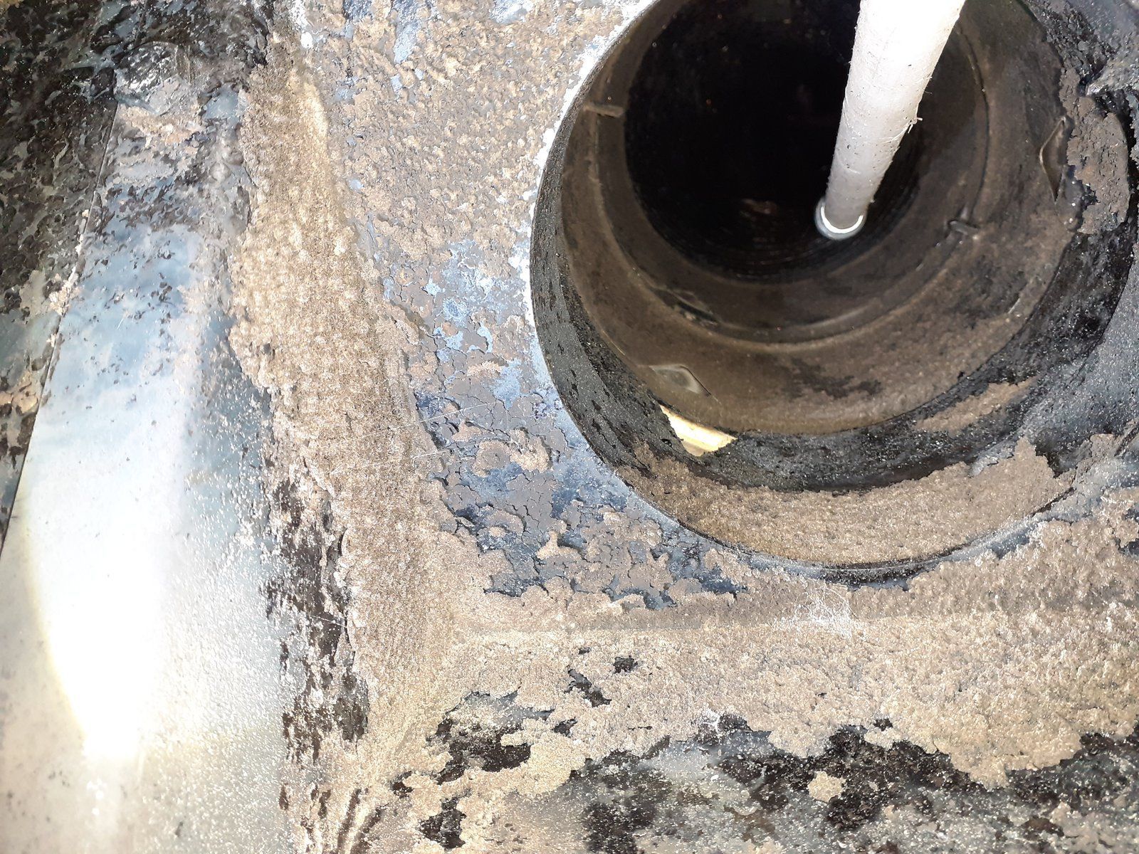 Gros plan sur l'ouverture d'un tuyau métallique sale, avec une tige blanche à l'intérieur et une surface environnante tachée de rouille.