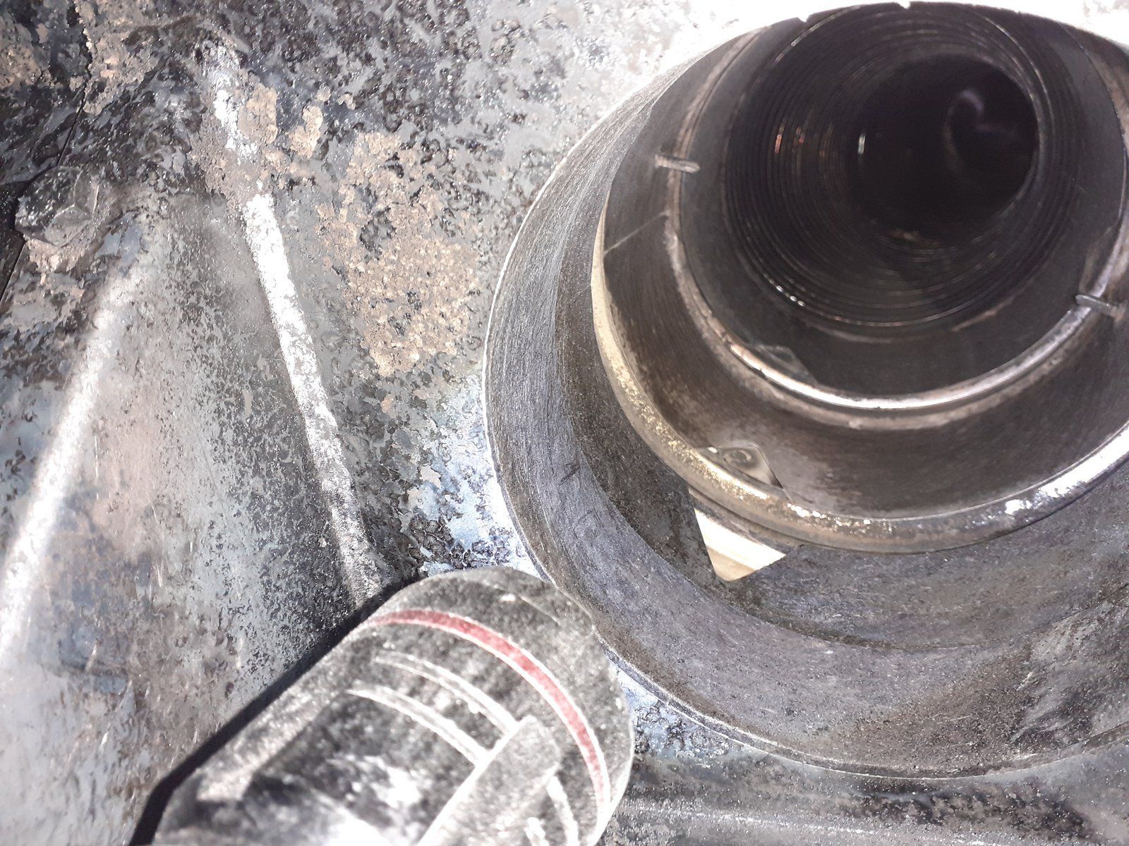Gros plan sur une pièce de moteur de voiture poussiéreuse, avec une ouverture circulaire noire et un tuyau bouché.