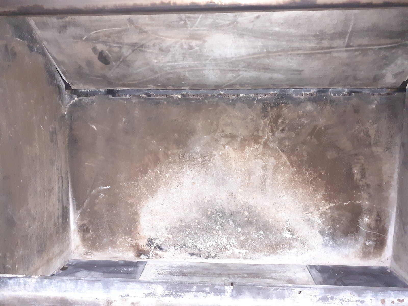 Intérieur d'une boîte métallique vide, présentant des surfaces grises usées et une légère décoloration.