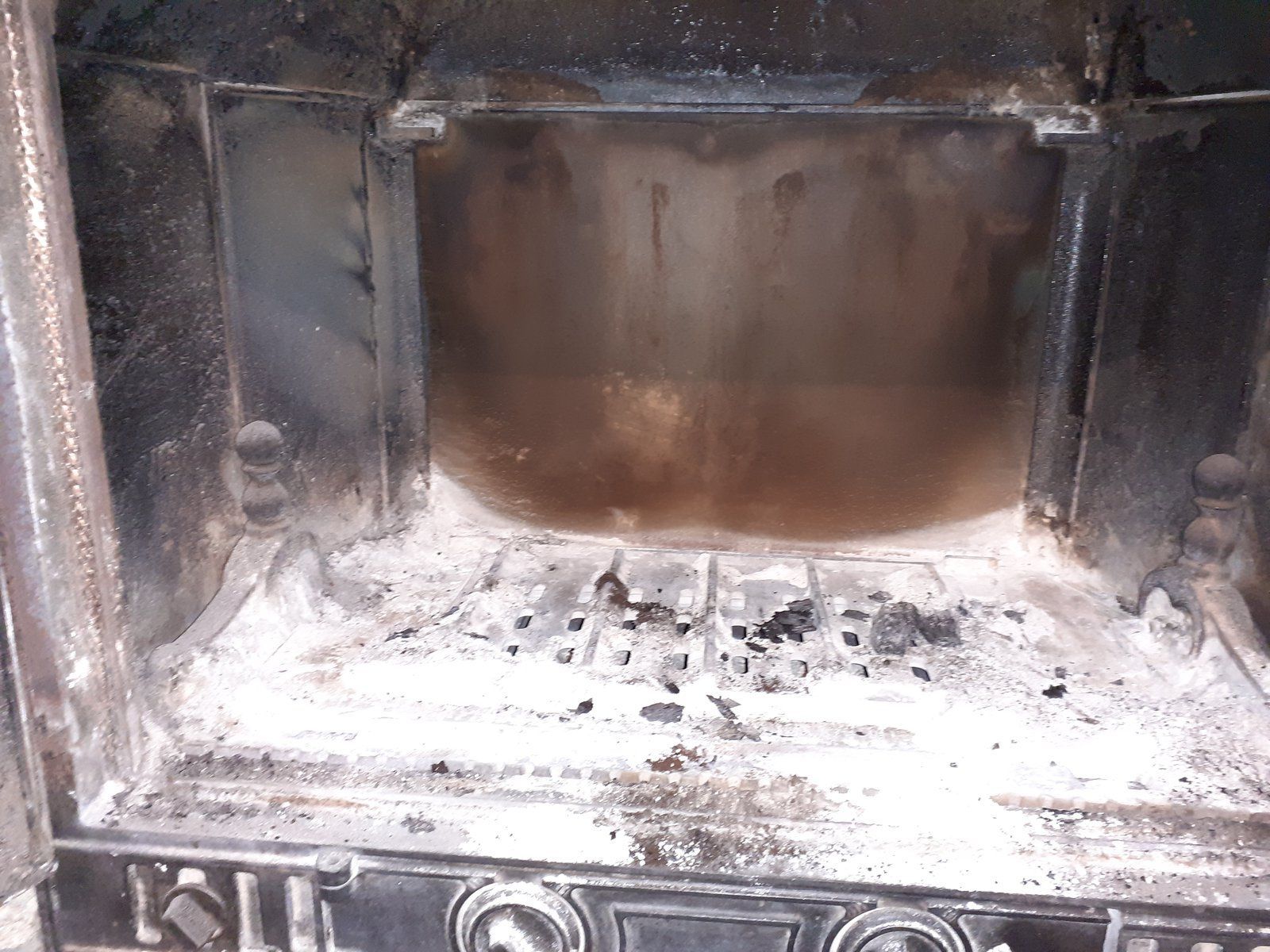 Cheminée noircie par la suie, avec un foyer recouvert de cendres et des bûches brûlées à l'intérieur d'un foyer en métal sombre.