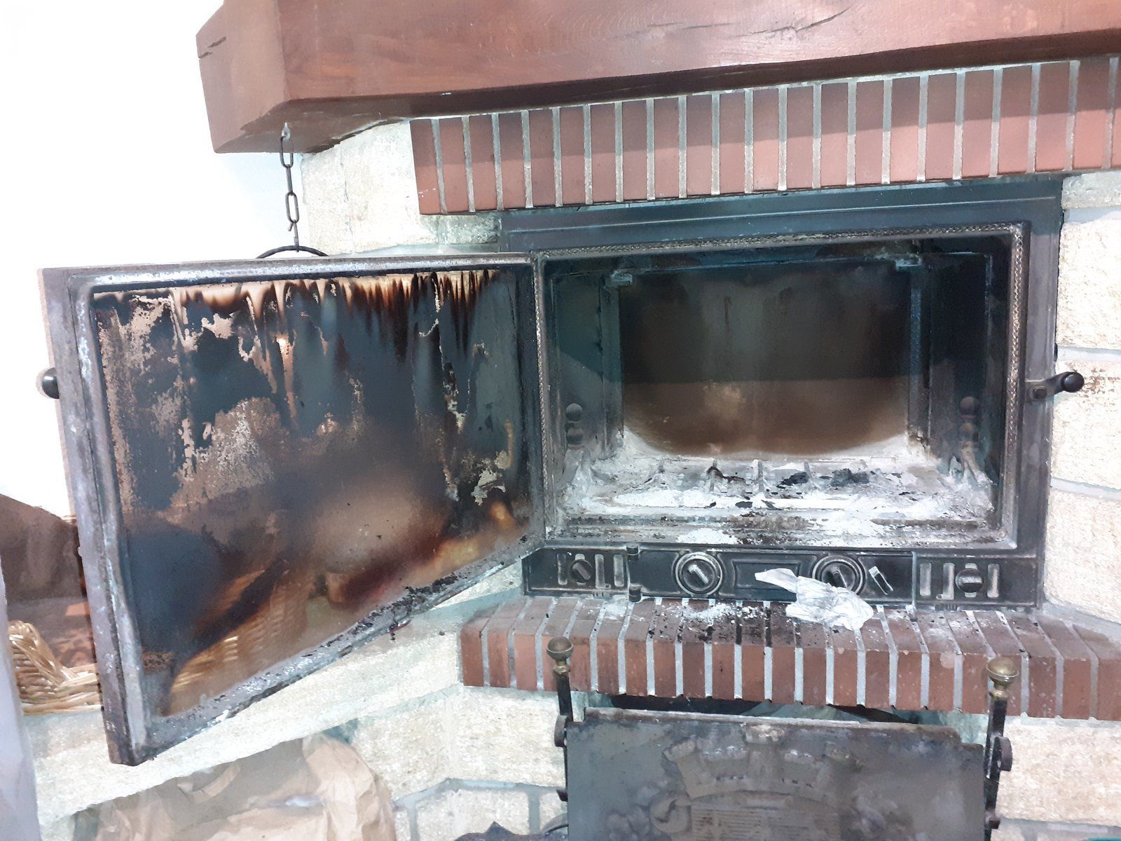 Insert de cheminée recouvert de suie, porte vitrée ouverte et dégâts causés par le feu à l'intérieur