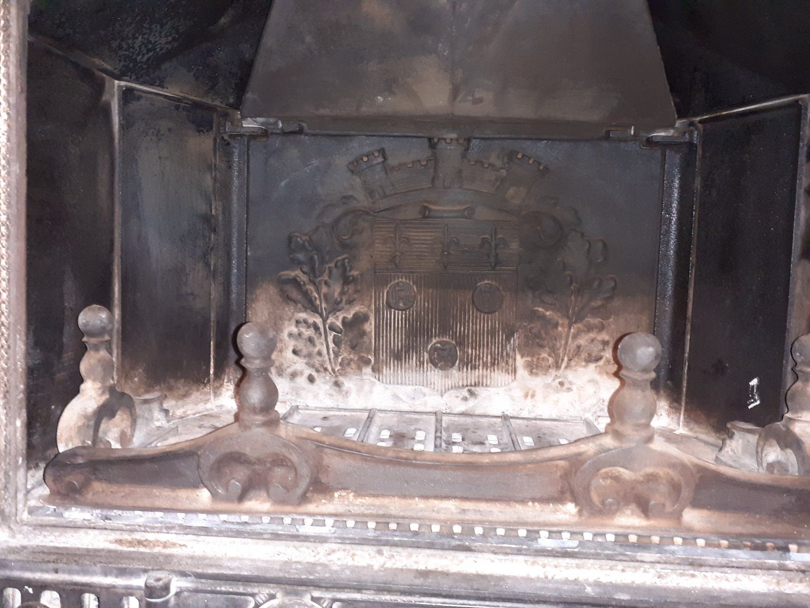 Une vieille cheminée avec un panneau arrière en métal noirci par la suie et des chenets à l'intérieur d'un foyer sombre.