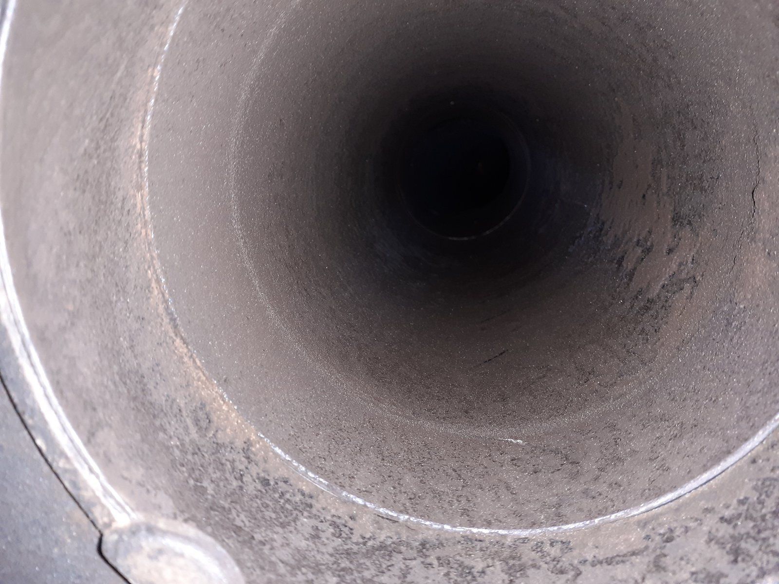 Gros plan sur l'intérieur d'un tuyau métallique gris présentant une ouverture circulaire sombre et une surface poussiéreuse.