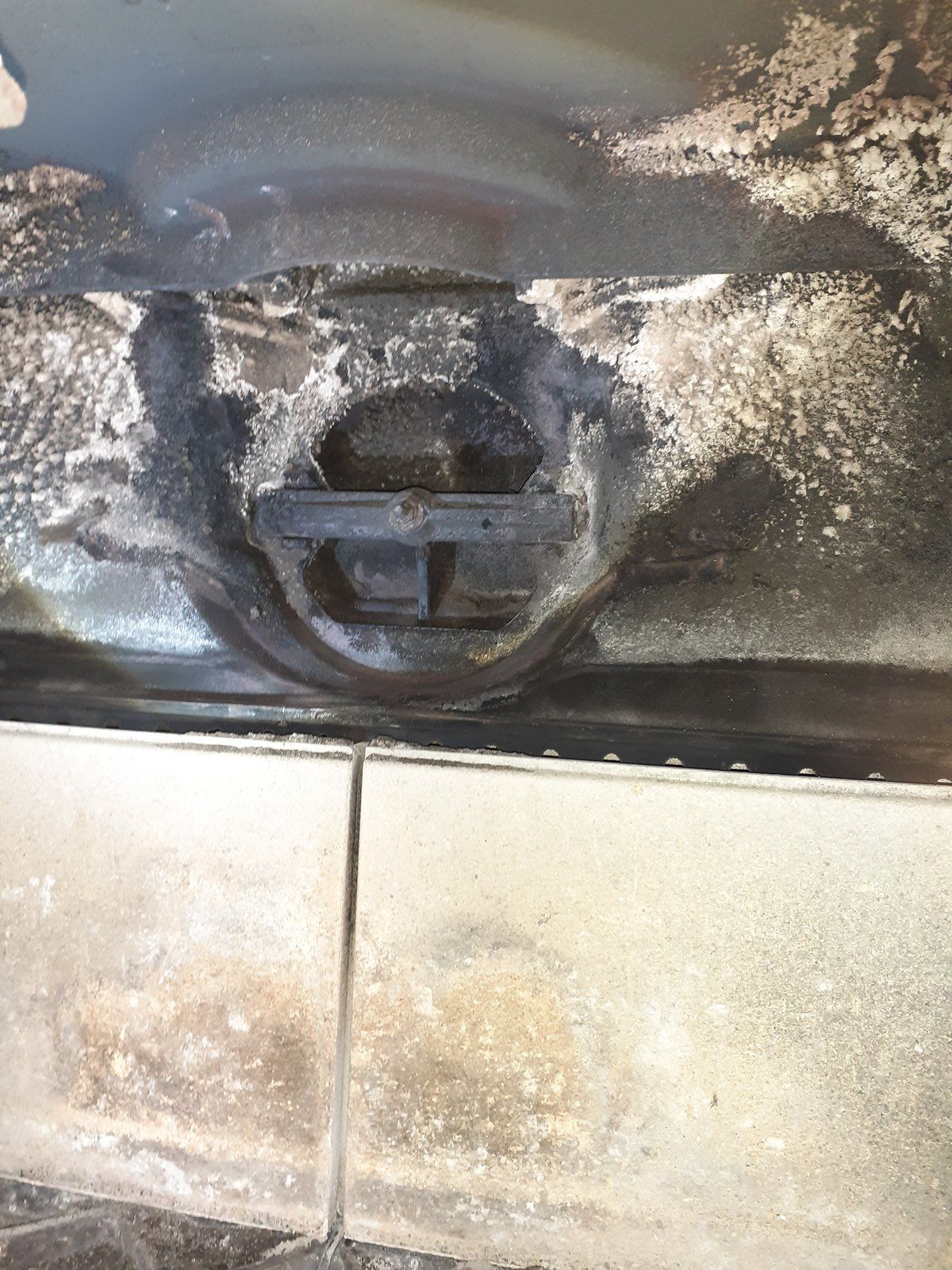 Gros plan sur une canalisation ou un conduit d'évacuation noir et beige sale, présentant des dépôts de crasse sur une surface carrelée.