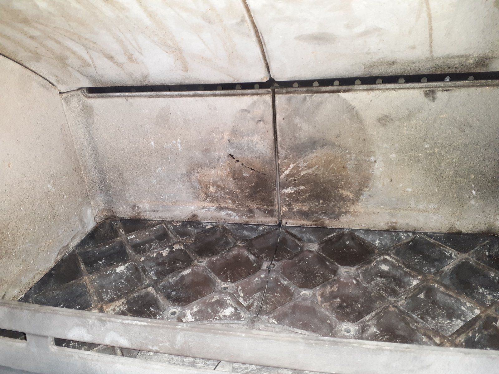 Intérieur du four ou du gril en métal sale avec des résidus brûlés et une grille de sol grasse à motif losange