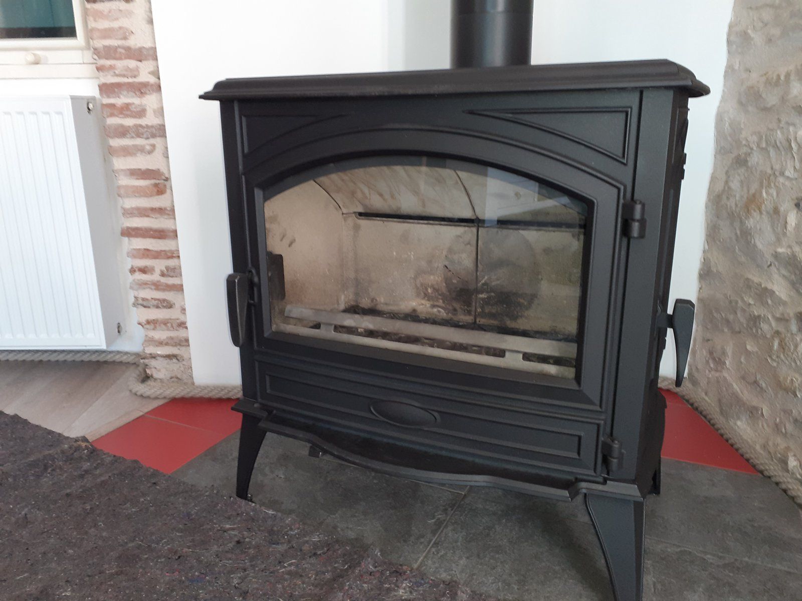 Poêle de cheminée en fonte noire avec porte vitrée dans une pièce aux murs de briques et de pierres.