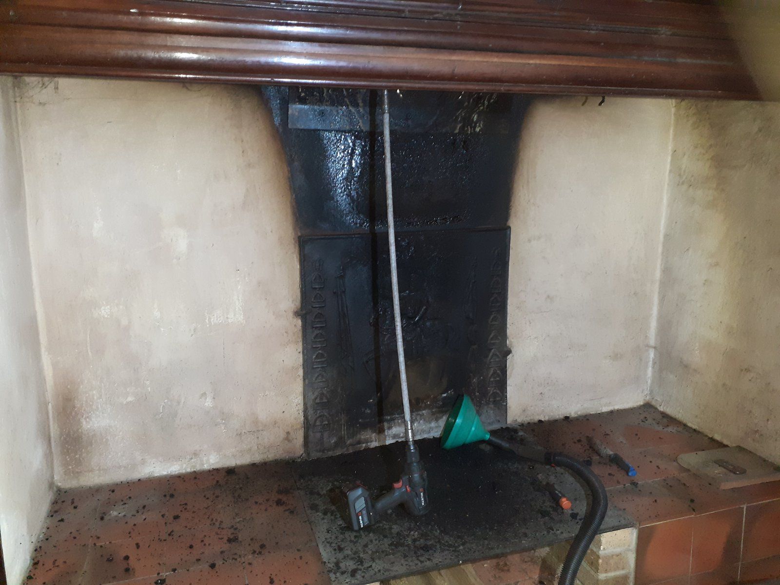 Cheminée avec une grille et un tisonnier en métal noir, et une pelle à poussière verte sur le foyer.