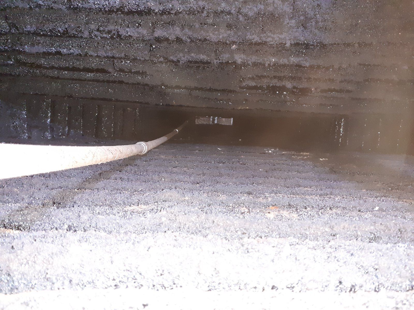 Dans un vide sanitaire sombre, un sol de gravier rugueux mène à une petite ouverture au fond.