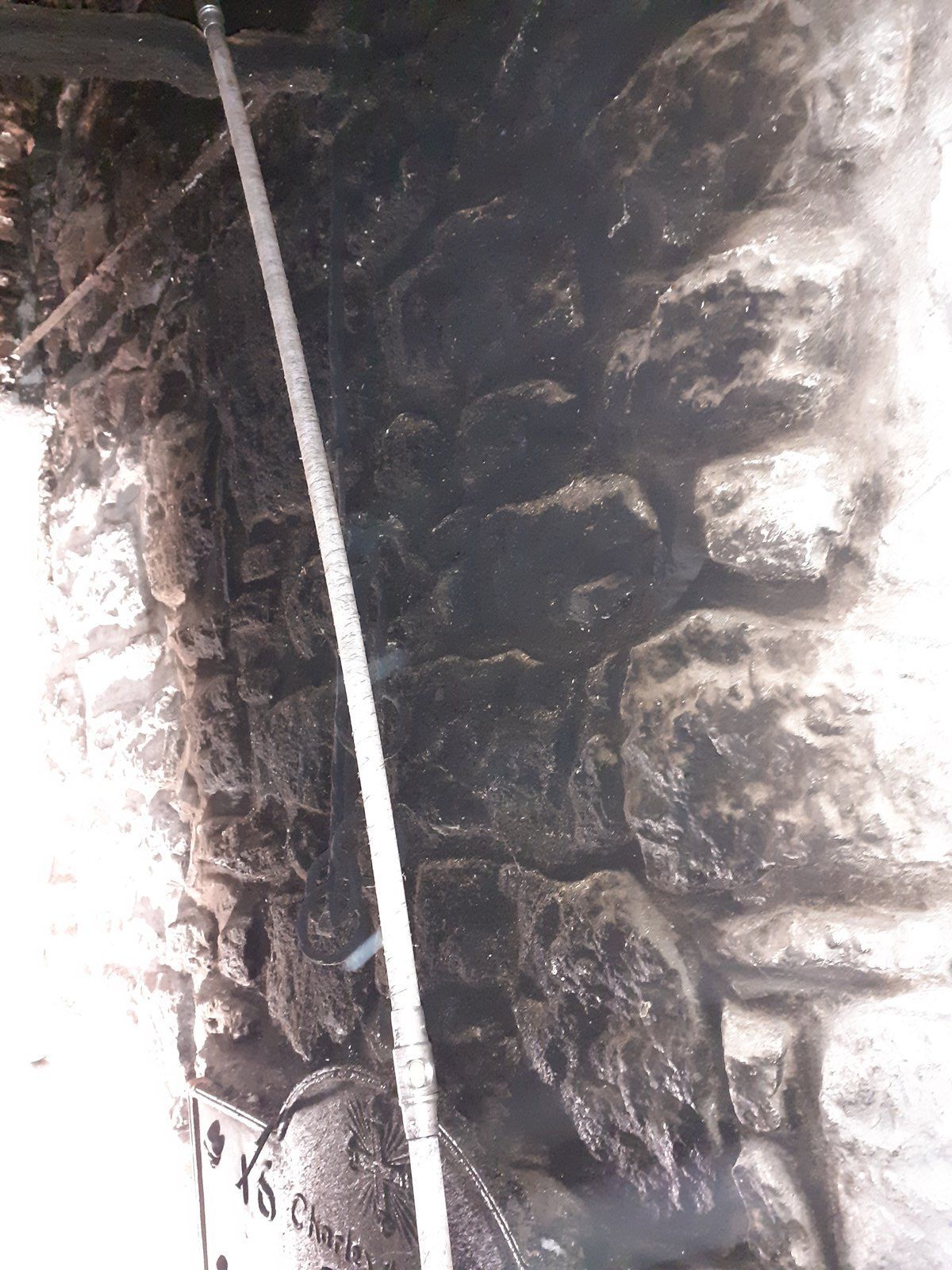Passage étroit et sombre en pierre, avec un poteau ou un tuyau blanc appuyé verticalement contre le mur.