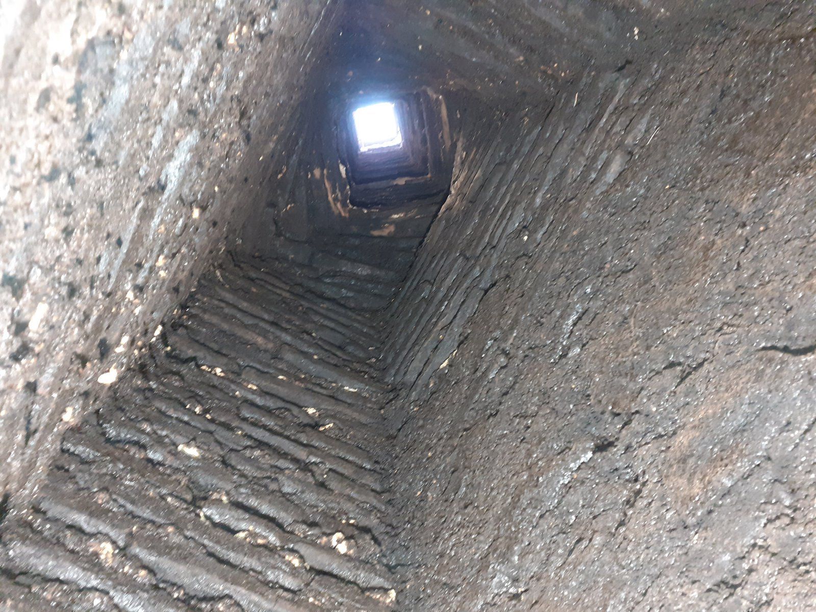 Tunnel ou puits revêtu de pierre avec une échelle menant à une ouverture lumineuse au-dessus