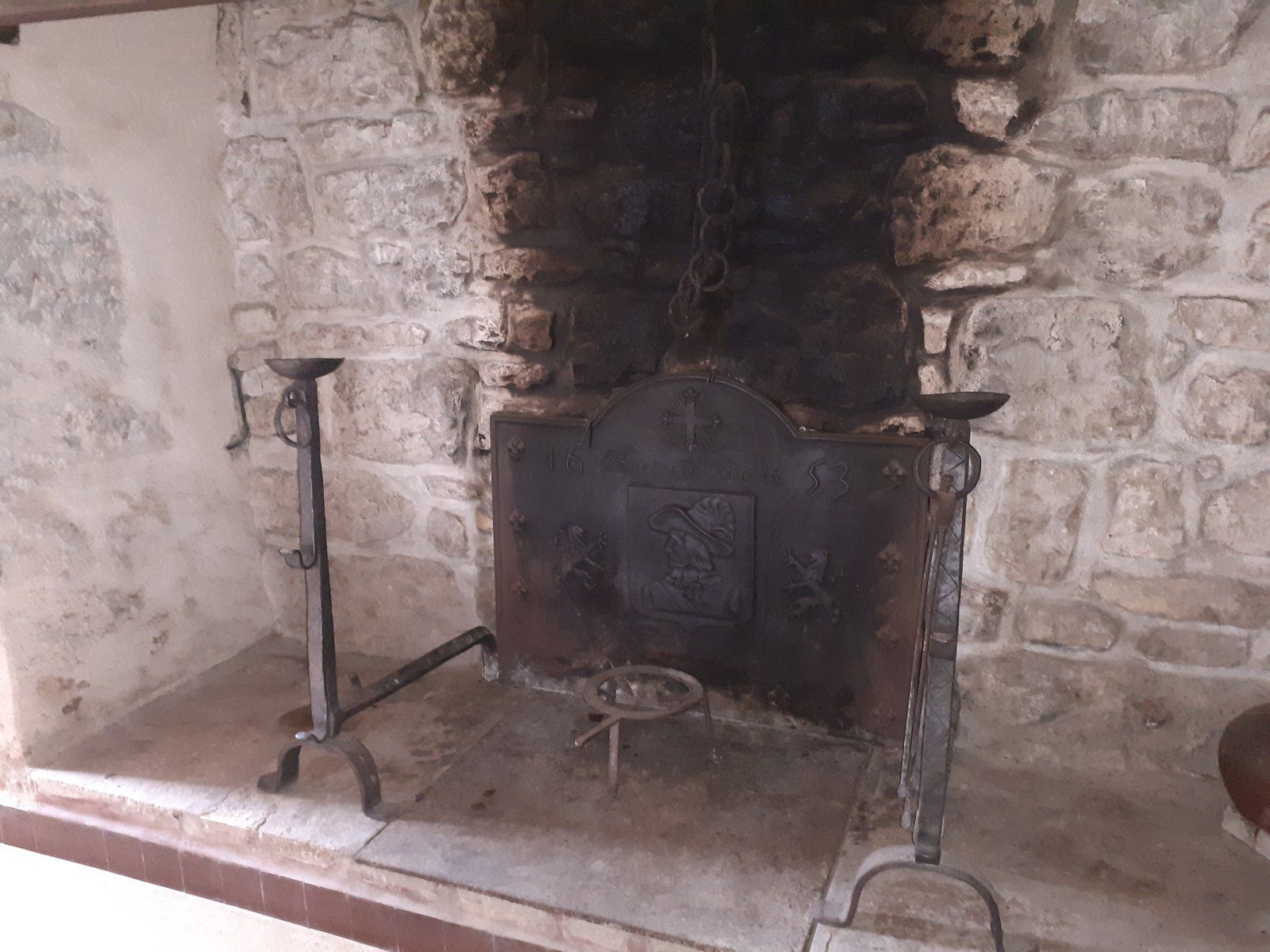 Vieille cheminée en pierre avec une grille en fer noir et un foyer noirci par la suie