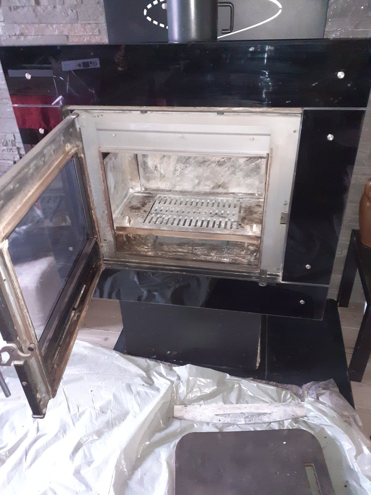 Porte de four ouverte, intérieur sale, dans un meuble de cuisine noir, à côté d'un évier et d'un plan de travail.