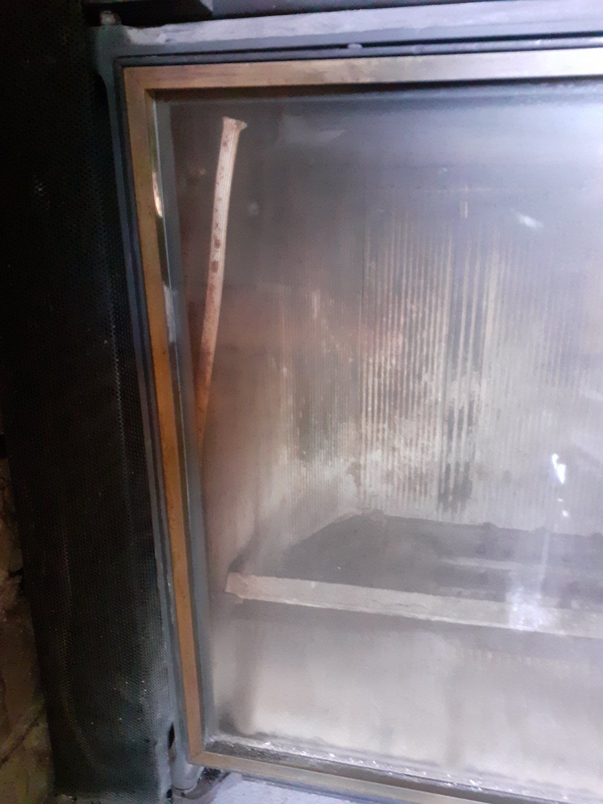 Gros plan sur une porte vitrée sale d'un appareil électroménager ou d'un meuble, présentant de la condensation et des traces.