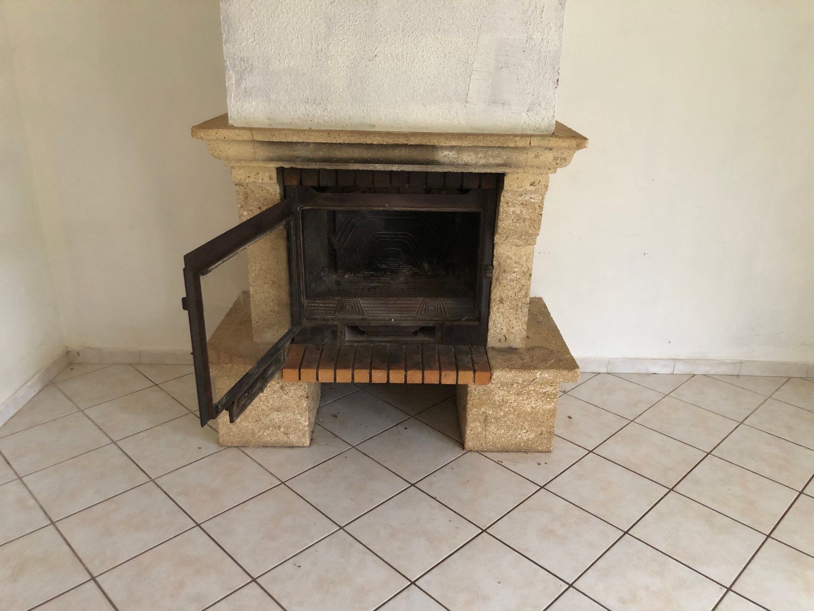 Une petite cheminée en pierre avec une porte noire ouverte dans une pièce carrelée.
