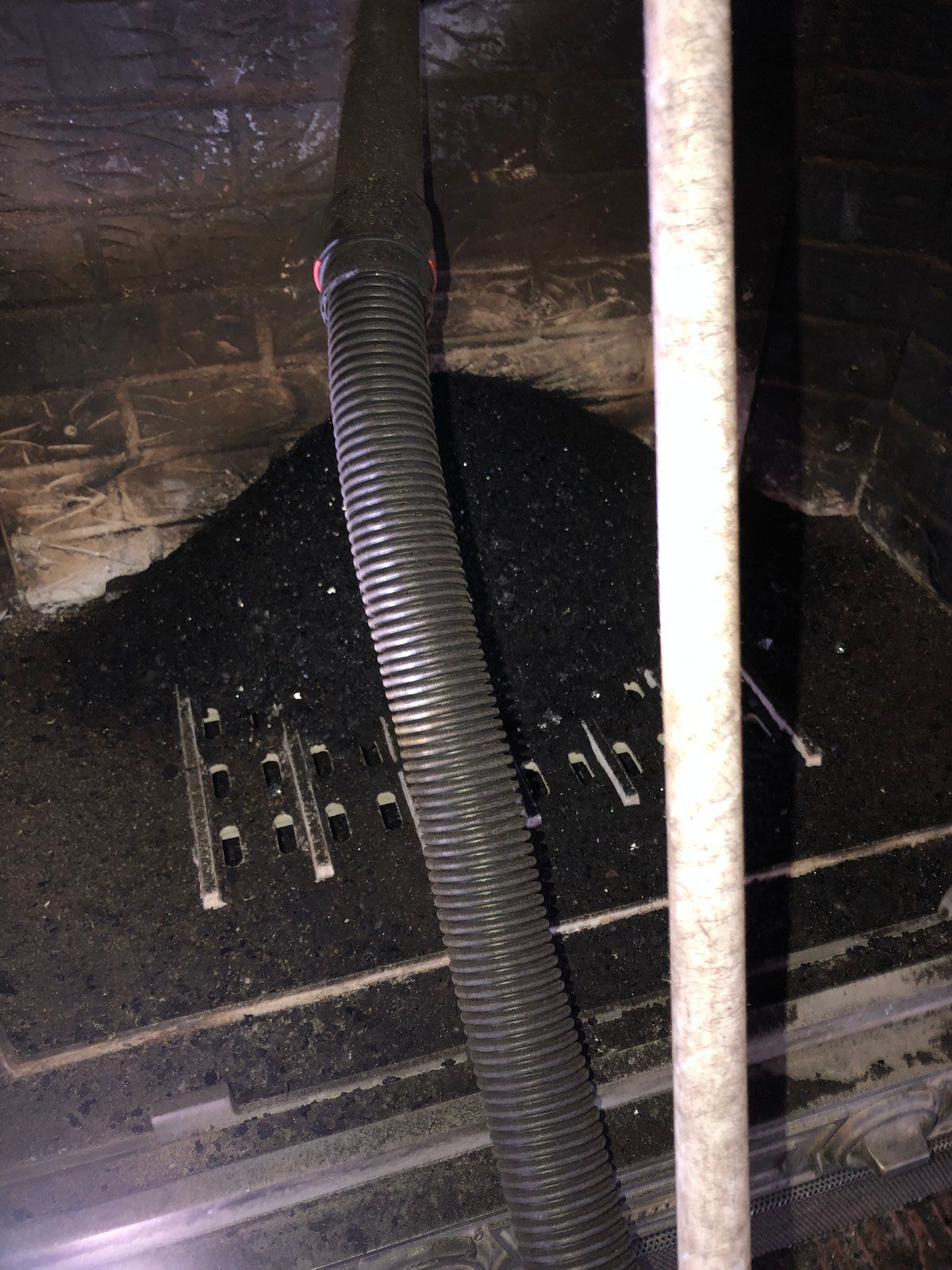 Intérieur d'une grille d'aération ou d'un conduit noir avec un tuyau ondulé et un tuyau blanc sur un mur sombre.