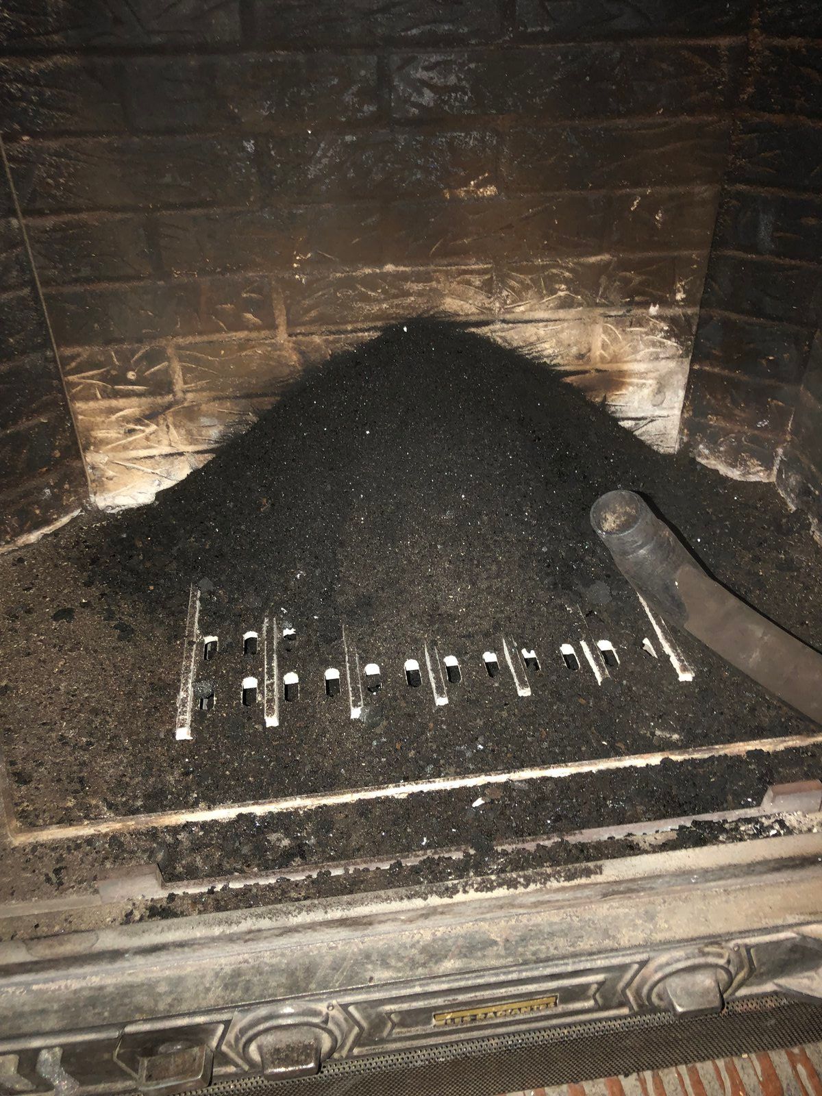 Cheminée avec un tas de charbon noir et un tisonnier en métal dans un foyer sombre.