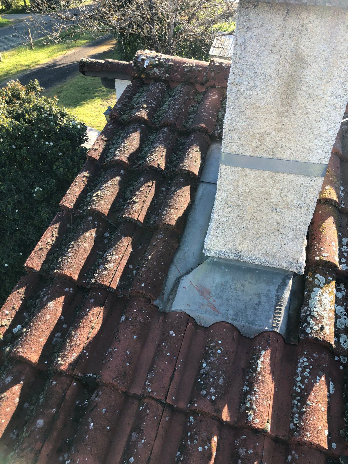 Des tuiles entourent une cheminée, la lumière du soleil projetant des ombres et de la mousse visible sur les tuiles.