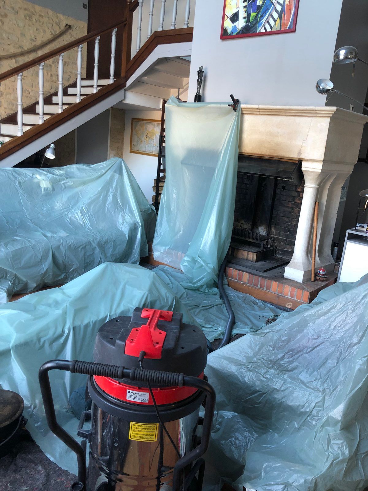 Salon avec meubles recouverts de bâches en plastique bleu autour de la cheminée et de l'escalier