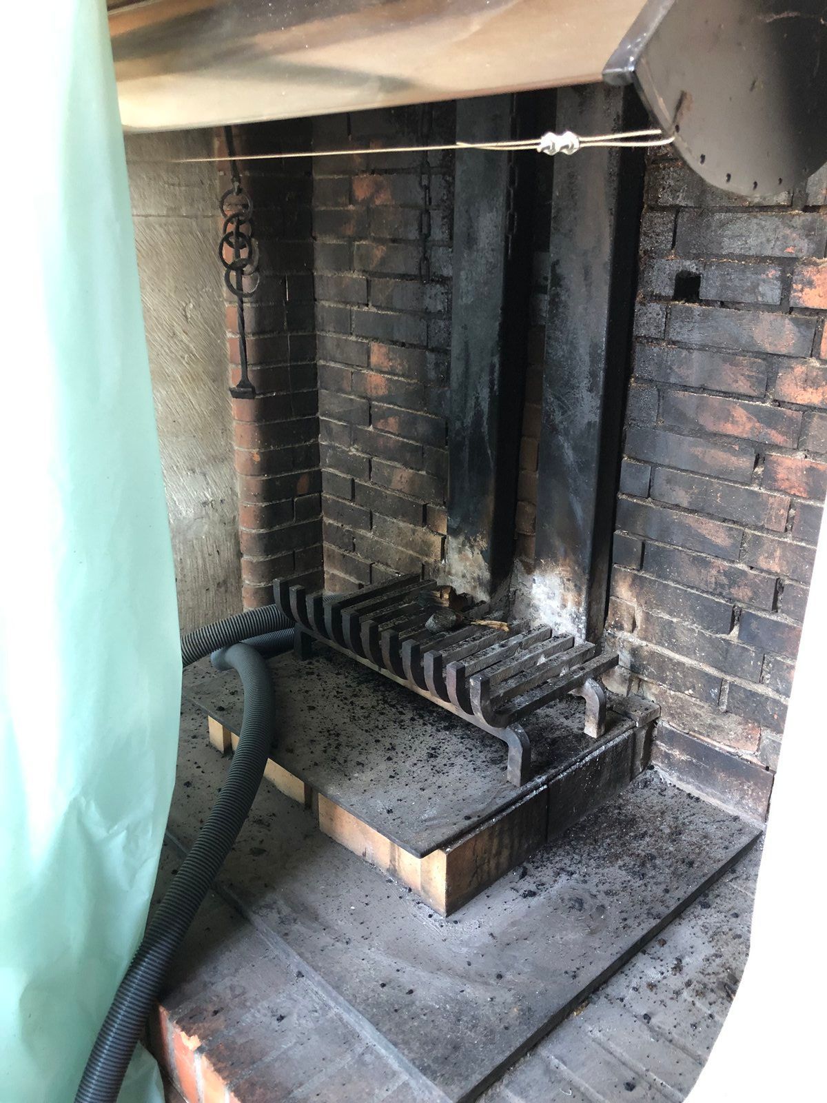 Cheminée en briques noircies par la suie, avec une grille métallique et un bac à cendres sous une barre de suspension.