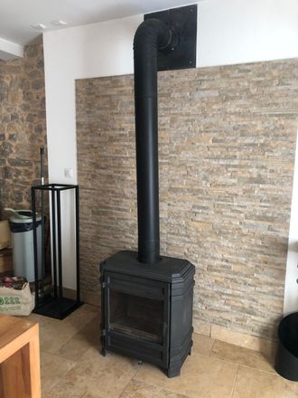Poêle à bois noir avec un haut conduit de fumée noir contre un mur à motifs de pierre dans une pièce