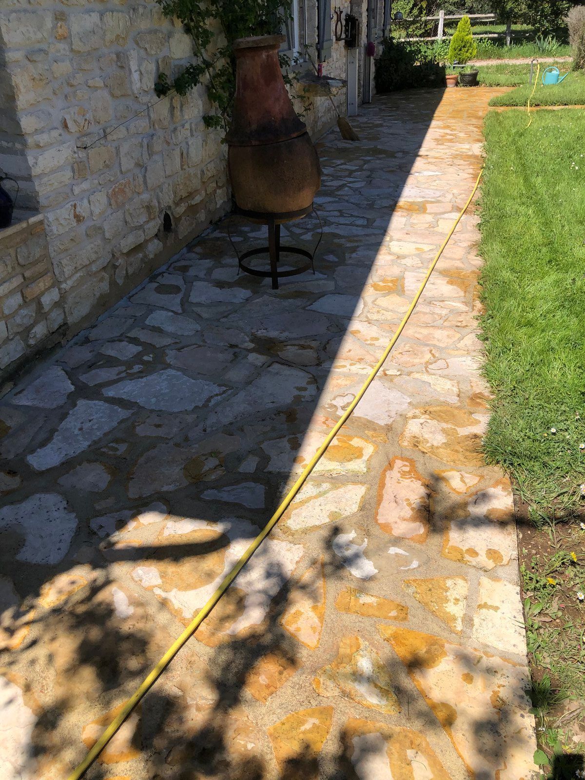 Allée en pierre longeant un mur de pierre, avec une pelouse et une grande cheminée d'extérieur à l'ombre.