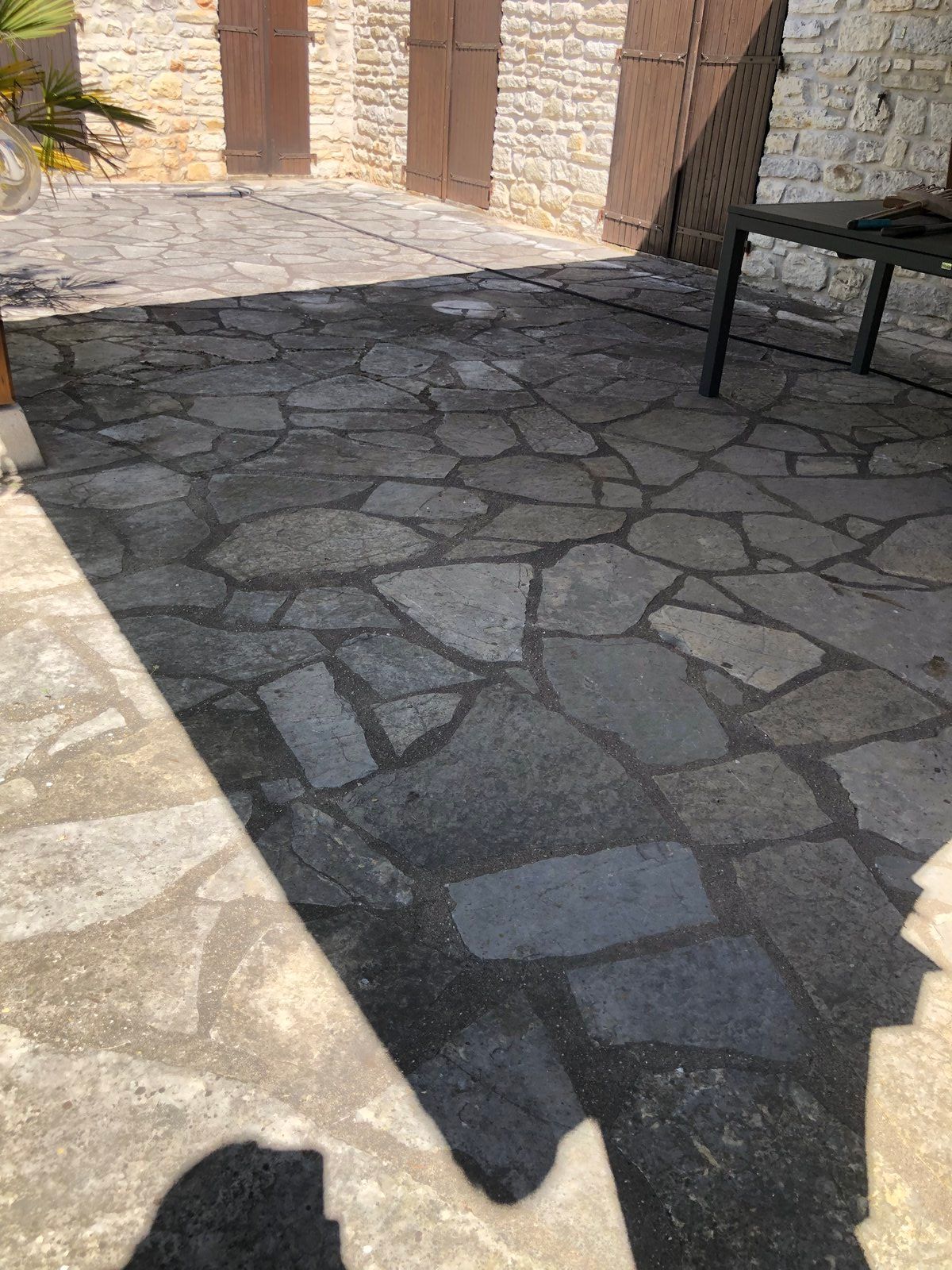 Cour pavée ensoleillée avec un banc et des ombres au niveau de la porte