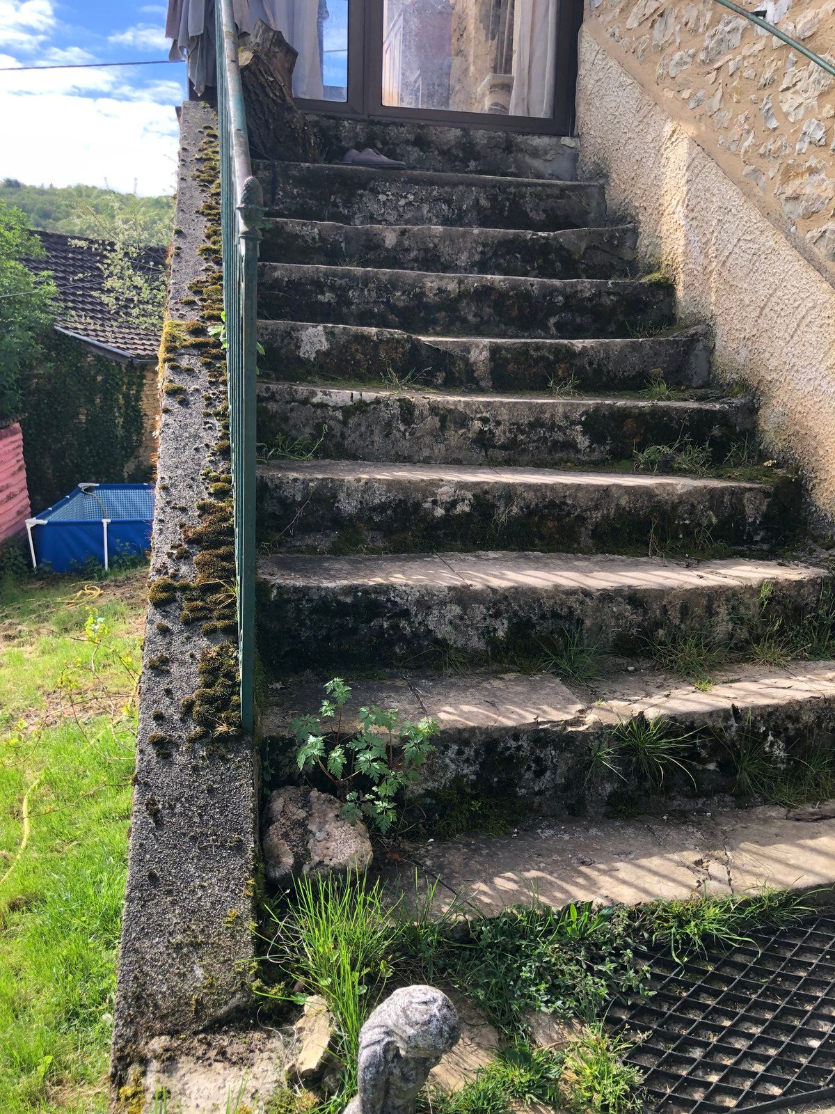 Escaliers extérieurs en pierre patinée, longeant un muret irrégulier, avec de l'herbe et un petit portail en haut.