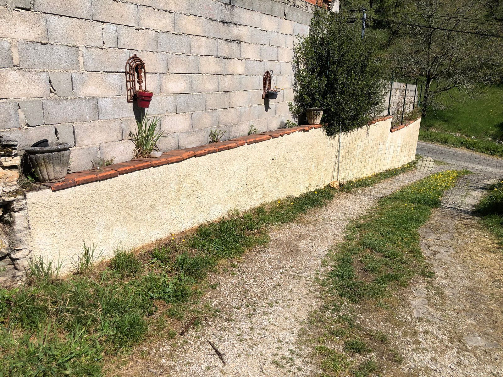 Chemin de gravier longeant un mur de pierre avec une borne d'incendie rouge et un petit arbre dans une cour de campagne