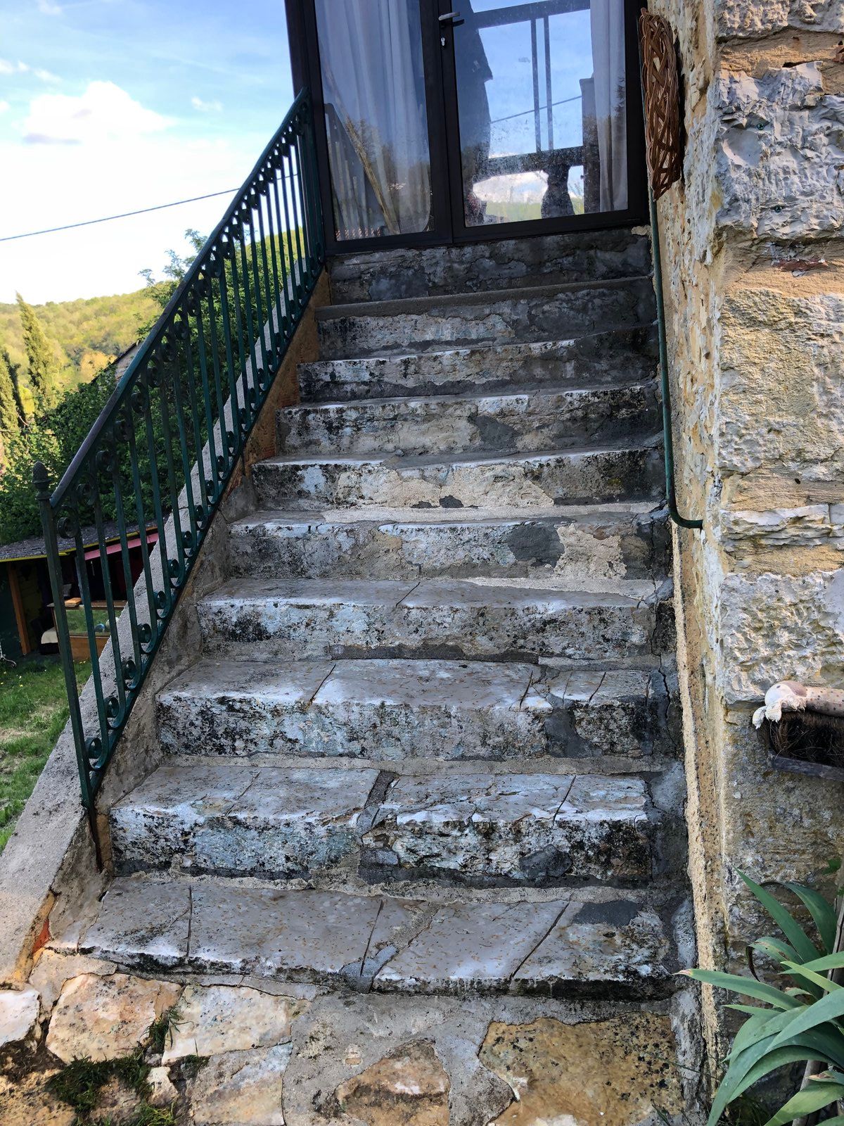 Escalier extérieur en pierre aux marches usées, rampe verte et porte en haut