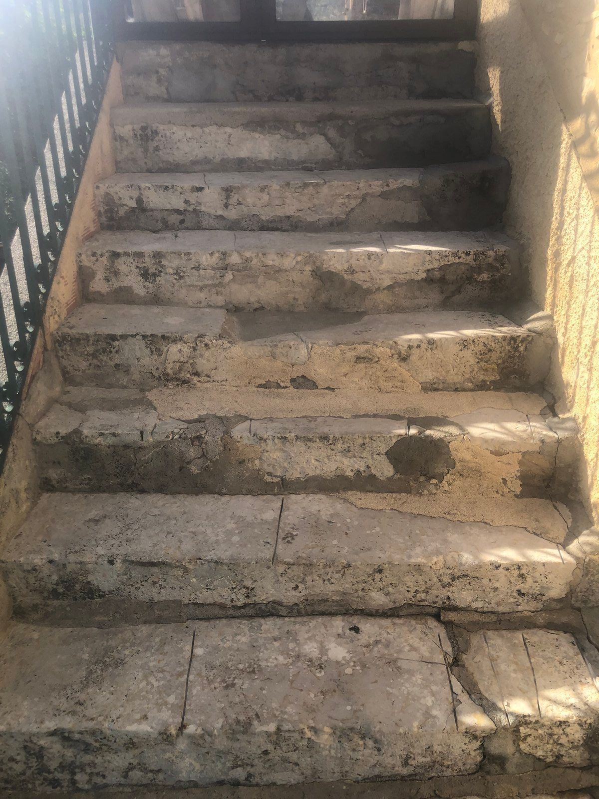 Escalier extérieur en béton avec marches usées et fissurées et une rampe métallique sur la gauche