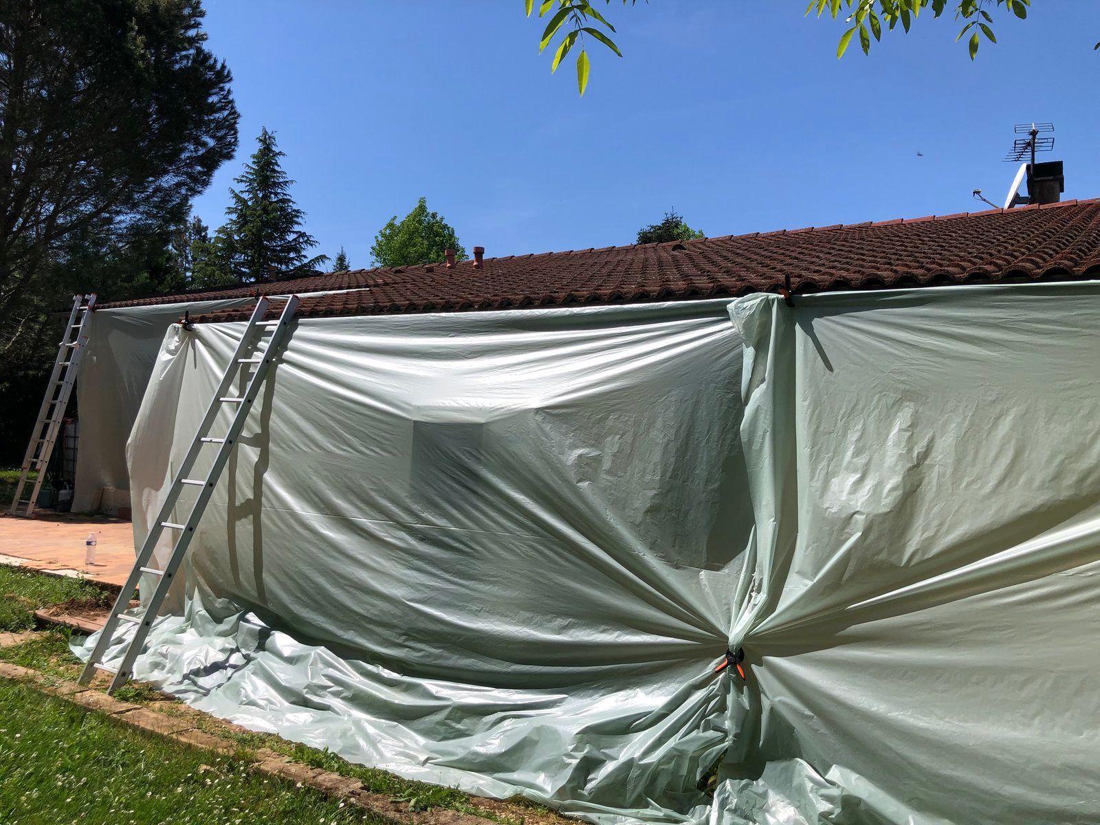 Une bâche blanche recouvre un bâtiment, des échelles sont appuyées contre lui, sous un ciel bleu.