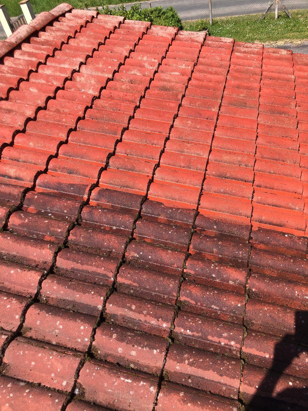 Des rangées de tuiles rouges, avec des tuiles plus foncées et abîmées par le temps au premier plan et de l'herbe en bordure supérieure.