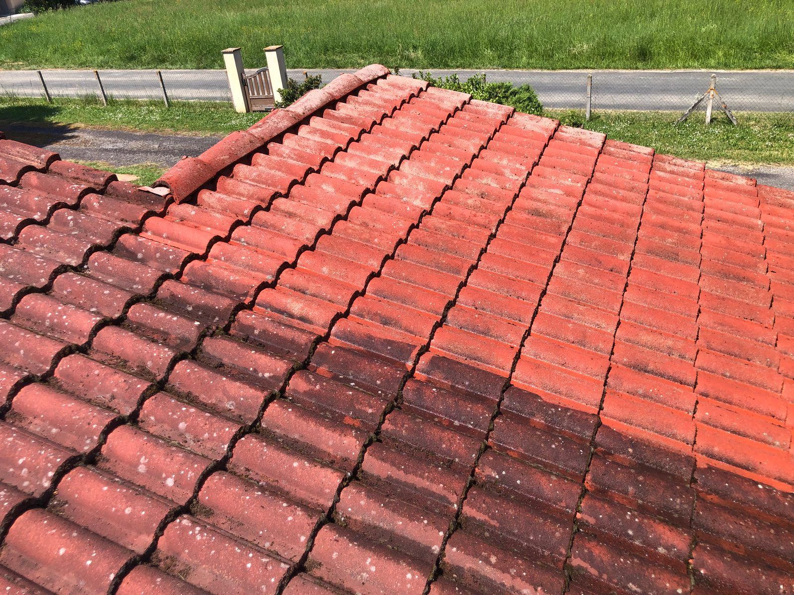 Toit de tuiles rouges et rouge foncé bordant une route et un chemin herbeux.